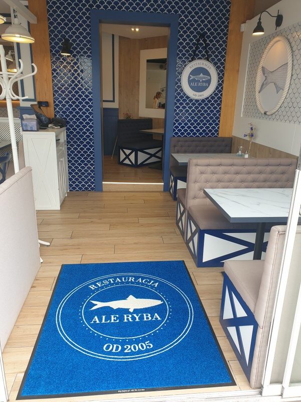 Niebieska mata z logo Restauracji Ale Ryba w wejściu do lokalu — realizacja BHP-Bejma