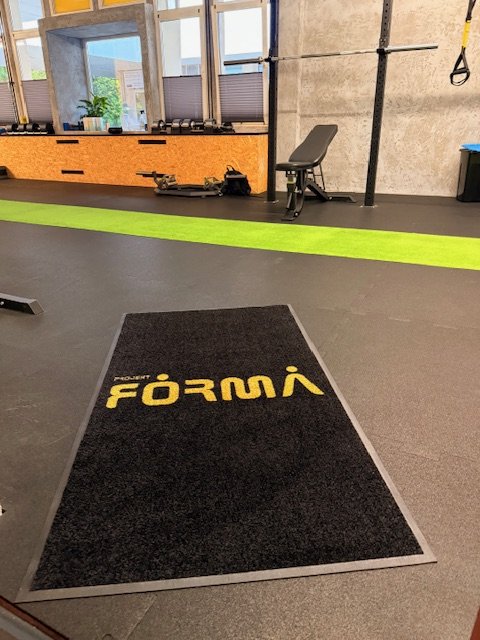 Czarna mata z żółtym logo siłowni Projekt Forma na posadzce sportowej — realizacja BHP-Bejma