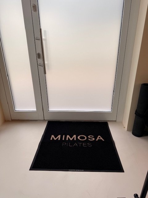 Czarna wycieraczka z logo Mimosa Pilates przy drzwiach wejściowych — realizacja BHP-Bejma